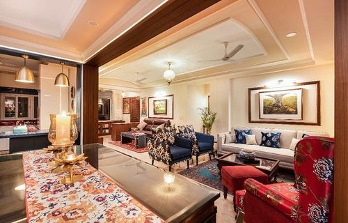 Eclectic living room with red wingback chair, navy patterned armchairs, framed art and layered rugs under warm lighting