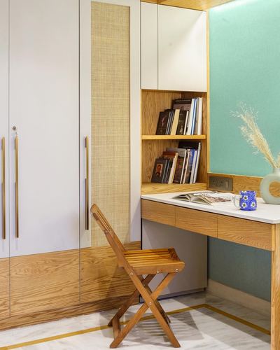 Study nook with wood desk, open shelf of books, cane panel wardrobe, teal wall and folding chair