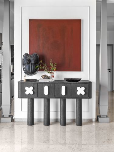 Dark wood console with cross cutouts beneath a large red painting in a white foyer