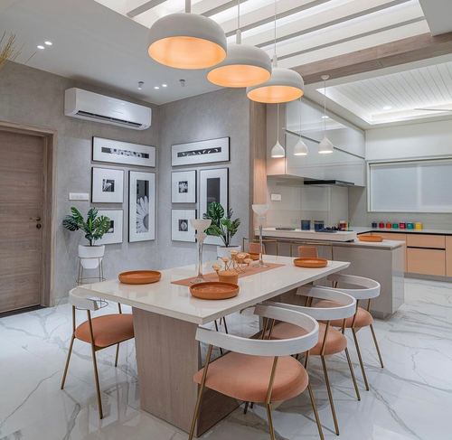 Dining table with peach curved chairs beneath dome pendant lights, open kitchen behind
