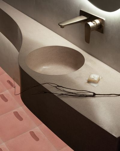 Curved concrete sink counter with wall faucet over terracotta patterned floor tiles