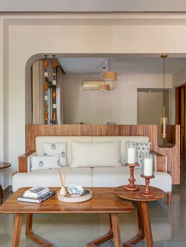 Arched teak opening frames a cream sofa with wooden coffee tables in a warm-toned living room