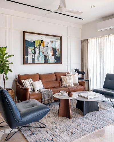 Living room with tan leather sofa, navy chairs, round coffee tables, and abstract art on panelled wall