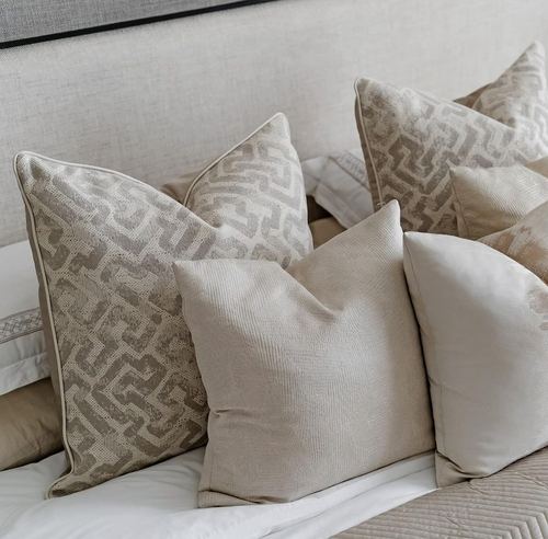 Close-up of layered beige and taupe textured pillows against an upholstered headboard
