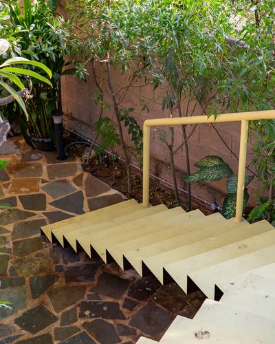 Outdoor stone staircase with yellow steps and handrail beside lush greenery and stone flooring