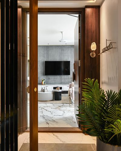 Open wooden door in foyer reveals living room with stone tv wall and marble floor