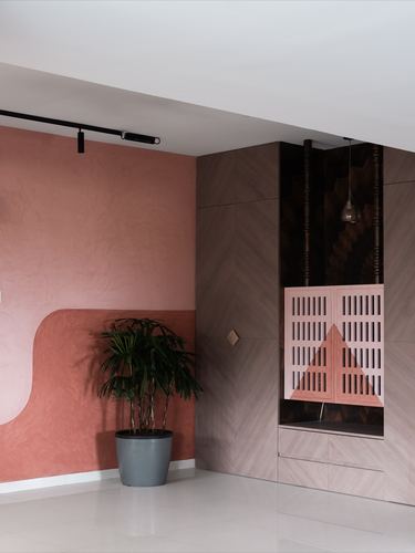 Terracotta plaster wall with curved motif beside a wood-panelled pooja niche with louvered doors