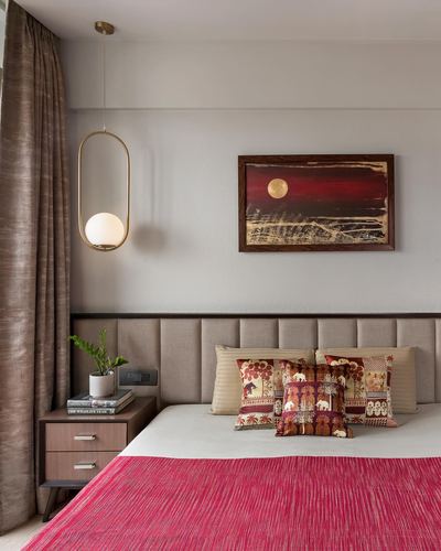 Bedroom with upholstered headboard, pink textured throw, brass pendant light, and framed sunset artwork.
