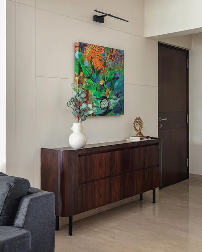 Wooden sideboard with vase and art beside a dark door in a minimal living room