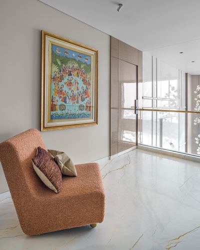 Terracotta boucle armchair beneath a gilt-framed pichwai painting in a marble-floored foyer