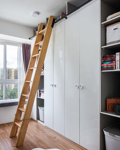Wooden rolling ladder against tall white wardrobe wall with open shelving and window seat