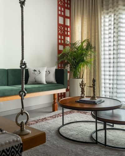 Green velvet swing beside round nesting tables with brass idols and a red lattice screen