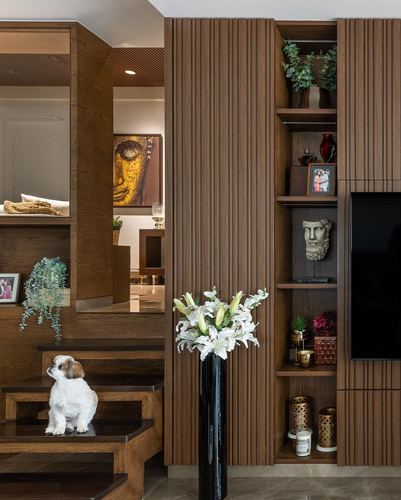 Fluted wood paneled living room wall with display niches, tv, lily arrangement, and a small dog on steps
