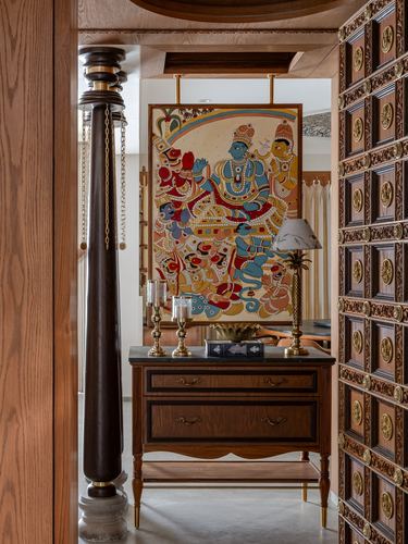 View through a carved wooden doorway to a console table beneath a suspended traditional Indian painting.