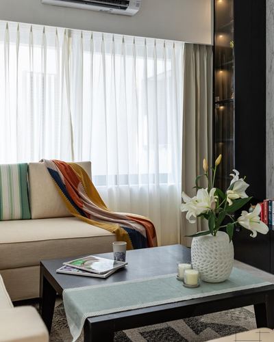 Beige sofa with colorful throw beside window, black coffee table with lilies and candles