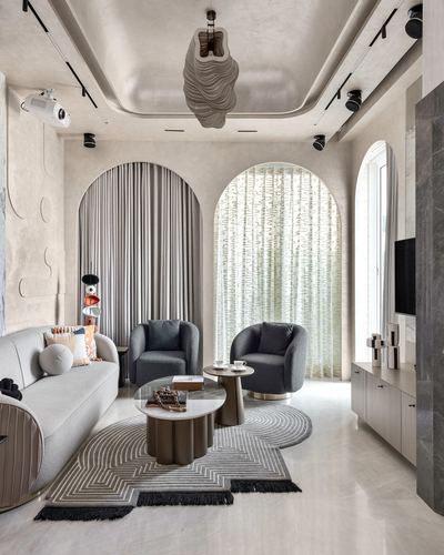 Living room with two curtained stone arches, charcoal armchairs, and a sculptural pendant light over a beige rug