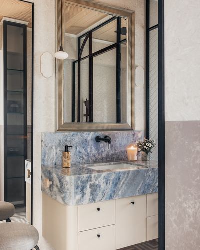 Bathroom vanity with blue-grey waterfall marble counter, black faucet, and framed mirror reflecting tiled shower