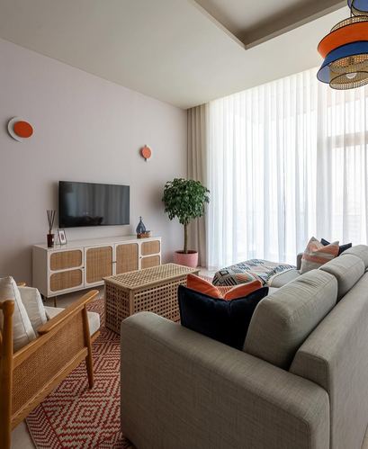 Living room with cane sideboard, sheer curtains, patterned rug, and orange wall sconces