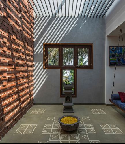 Sunlit courtyard foyer with brick wall, wooden window, stone pedestal and floral urli on patterned floor