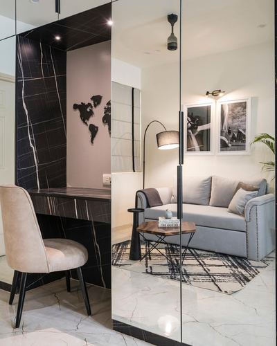 Black marble console nook beside glass-partitioned living room with gray sofa and arc lamp