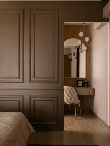 Doorway through dark paneled wall reveals wood vanity with arched mirror and globe pendants