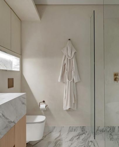 Minimalist bathroom with marble vanity, wall-hung toilet, and robe hanging beside glass shower