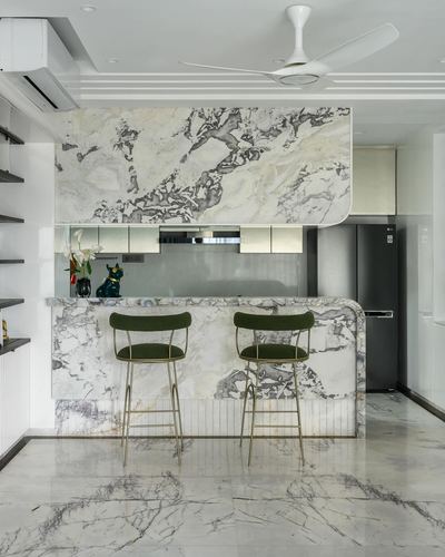 Mumbai kitchen with veined marble counter, arched marble overhang, and olive velvet bar stools