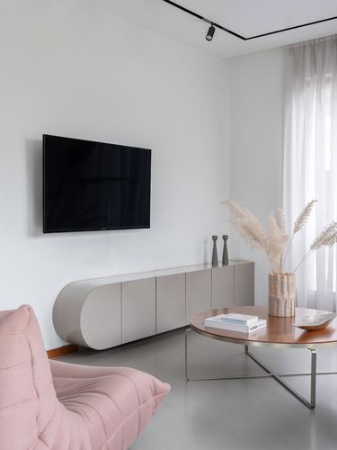 Minimalist living room with pink lounge chair, curved credenza, wall tv, and round wood coffee table