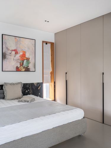 Minimalist bedroom with grey bedding, dark stone headboard, abstract art, and tall beige wardrobes