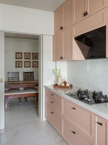 Blush pink kitchen with stone backsplash opening to a dining room with framed prints