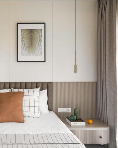 Bedroom corner with tufted headboard, fluted nightstand, brass pendant, and framed architectural print