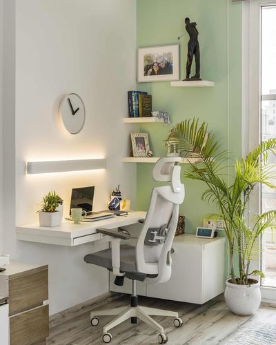 Small home office corner with white ergonomic chair, floating desk, sage green wall and potted palm