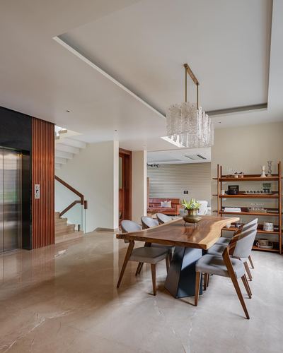 Open dining area with live-edge wood table, grey chairs, glass chandelier and staircase beyond