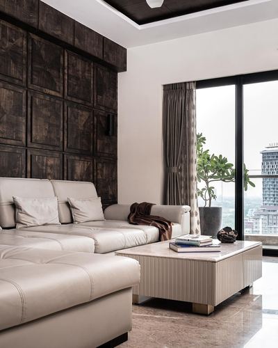 Living room with beige sectional sofa, dark carved wood wall panel, and city skyline through glass doors