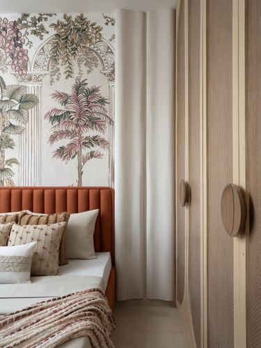 Bedroom corner with terracotta channel headboard, botanical mural wall, and fluted wood wardrobe with round pulls