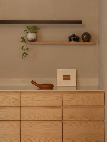 Wood-grain kitchen cabinetry with a floating shelf of ceramics above stone countertop
