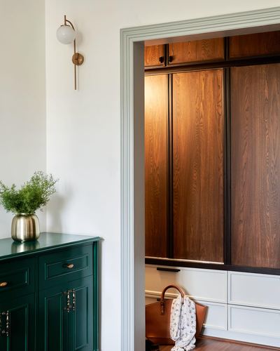 Foyer with green lacquered cabinet, brass sconce, and open wardrobe with wood-paneled doors and a leather bag.