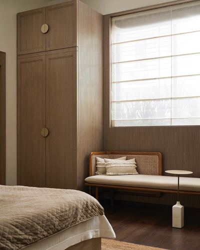 Wooden wardrobe with round brass pulls beside cane bench under a window in a bedroom