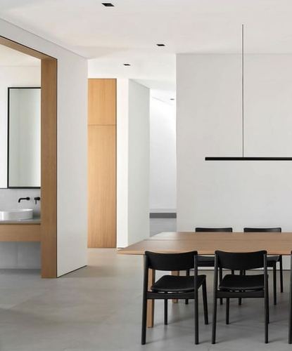 Minimalist white dining area with black chairs and wood table, glimpse into bathroom through wide doorway
