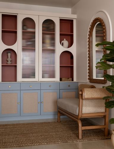 Cream and blue cabinetry with arched terracotta niches, cane armchair, and beaded arched mirror