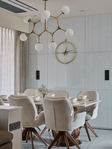 Beige dining set under a branching globe chandelier against a paneled wall with a large clock