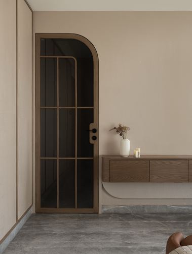 Arched glass door beside floating wood console with vase on grey marble floor