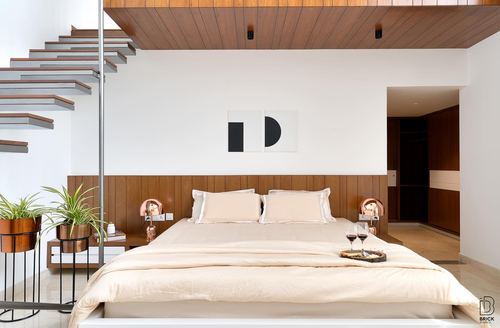 Neutral bedroom with wood-panelled headboard wall, floating staircase, and wine tray on bed