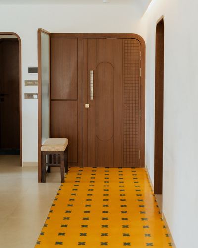 Arched wooden entry door beside mustard patterned tile runner in curved foyer corridor