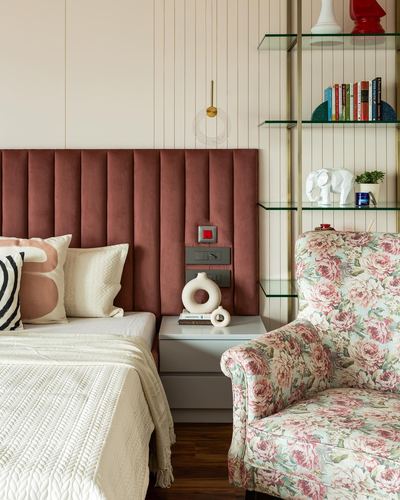 Bedroom corner with pink channel-tufted headboard, glass shelving unit, and floral armchair
