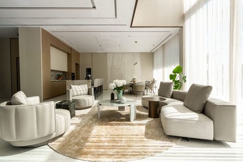 Open-plan living and dining space with cream sectional, round rug, and floor-to-ceiling sheer curtains