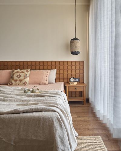 Bedroom with grid-paneled wood headboard, pink linens, cane pendant light, and sheer curtains beside window