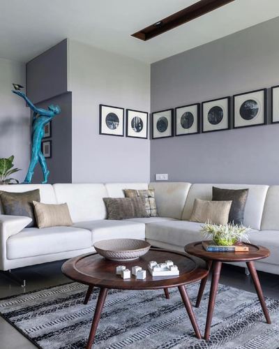 Grey living room with white sectional, round wood coffee tables, and a blue patina sculpture near the entrance