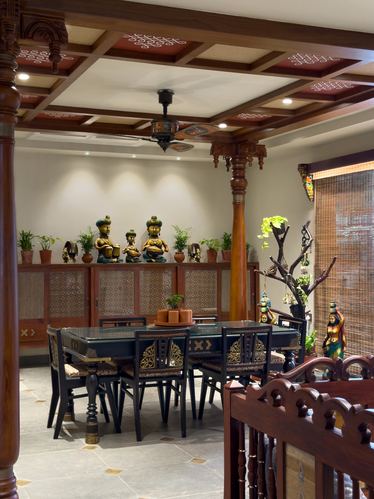 Traditional South Indian dining room with carved wooden pillars, coffered ceiling, and brass figurine display