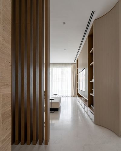 Fluted wood partition beside a curved shelving wall leading into a sunlit minimalist lounge